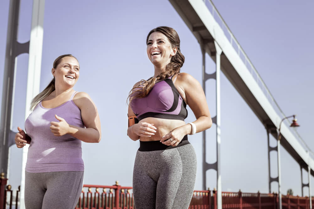 Two curvy women in their sportswear, running under the bridge
