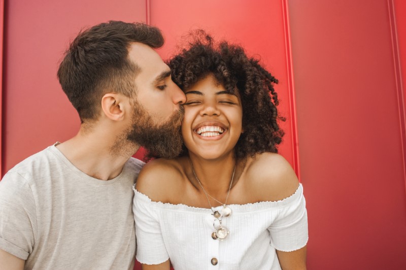 happy interracial couple cheek kiss